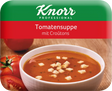 Tomatensuppe mit Croutons in weißer Schale, frische Tomaten im Hintergrund