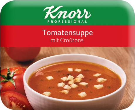 Tomatensuppe mit Croutons in weißer Schale, frische Tomaten im Hintergrund
